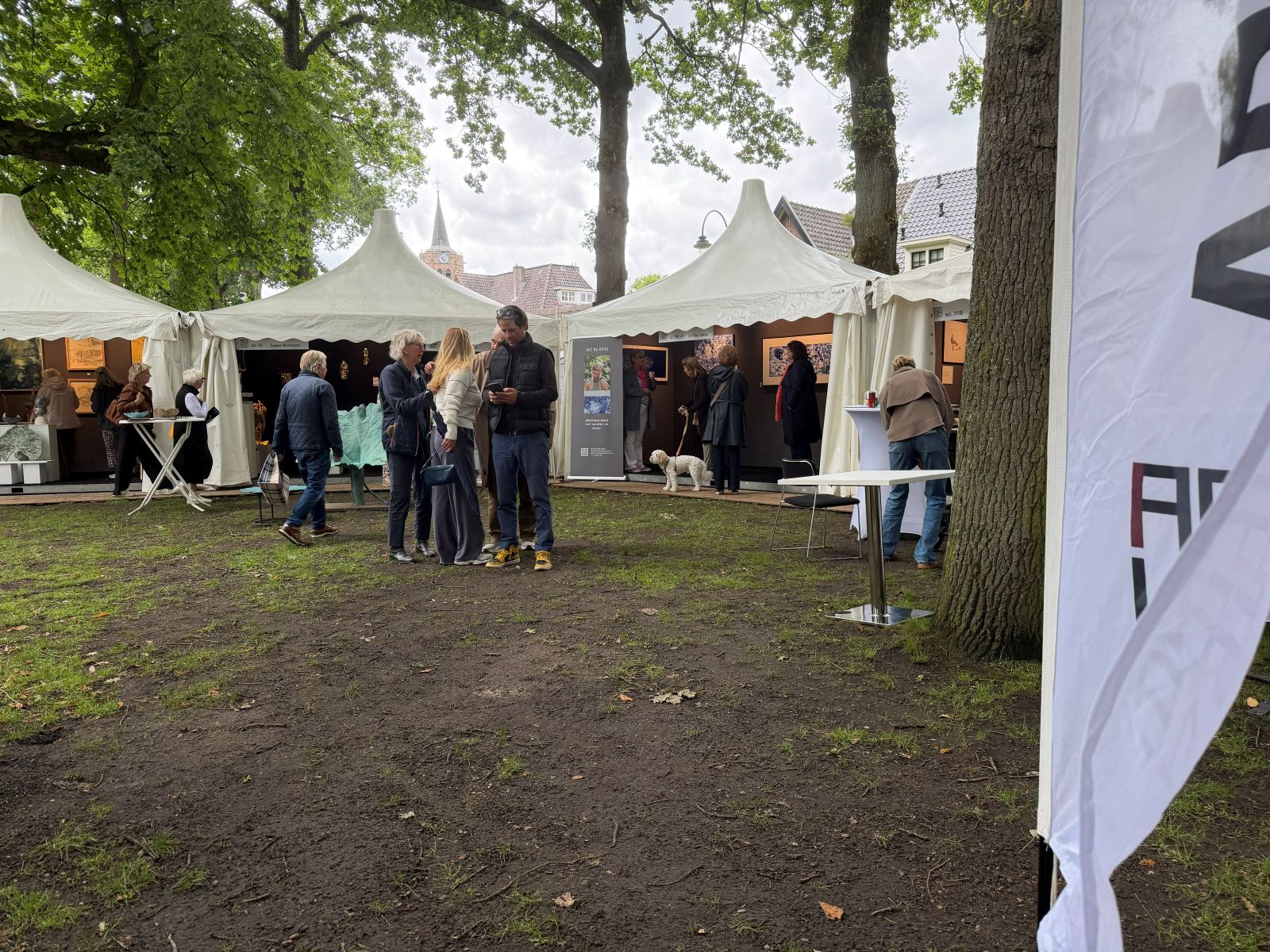 "Openlucht kunstbeurs Art Laren 2026 op de Brink met witte paviljoens en bezoekers tussen de bomen"